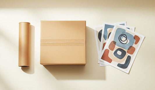 Plain shipping box, mailing tube, and stack of art prints arranged in three groups